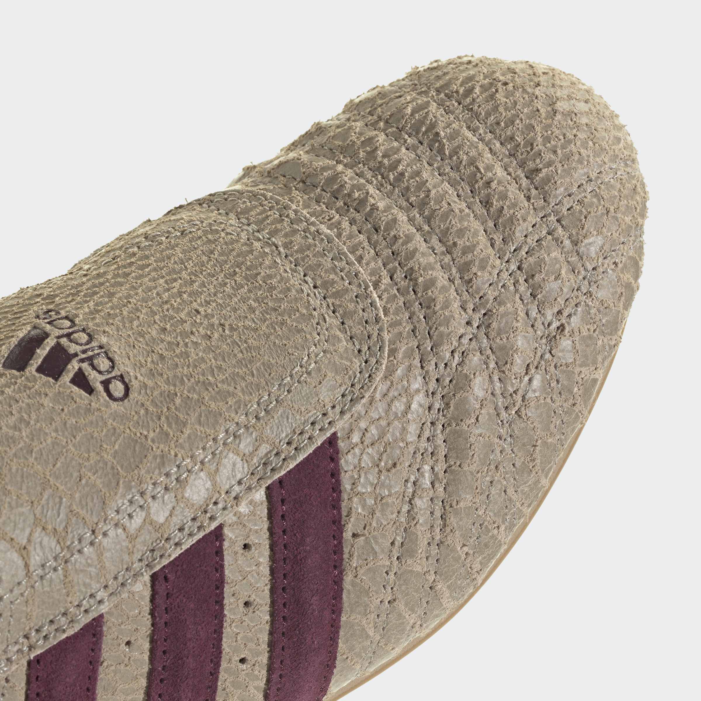 תקריב נעל סניקרס טקסטורת עור בז', עם פסים סגולים בעיצוב ספורט אלגנטי