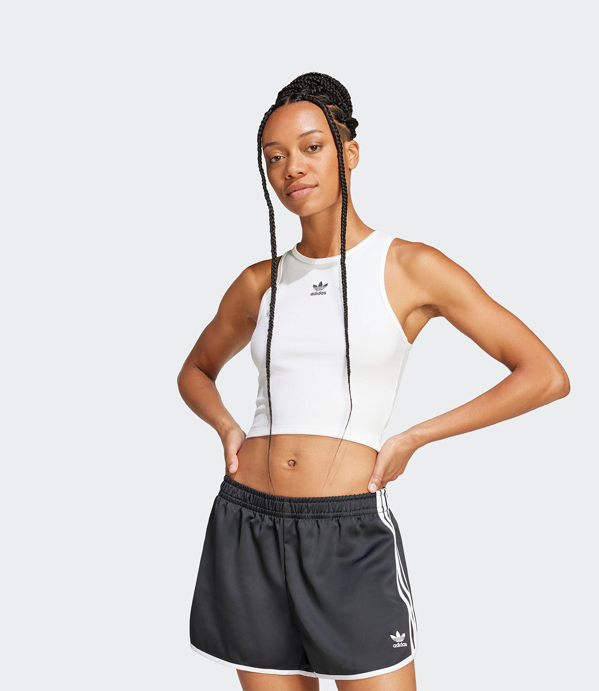 אישה לובשת גופיית ספורט לבנה ומכנסי ספורט קצרים בצבע שחור עם פסים לבנים, רקע אפור