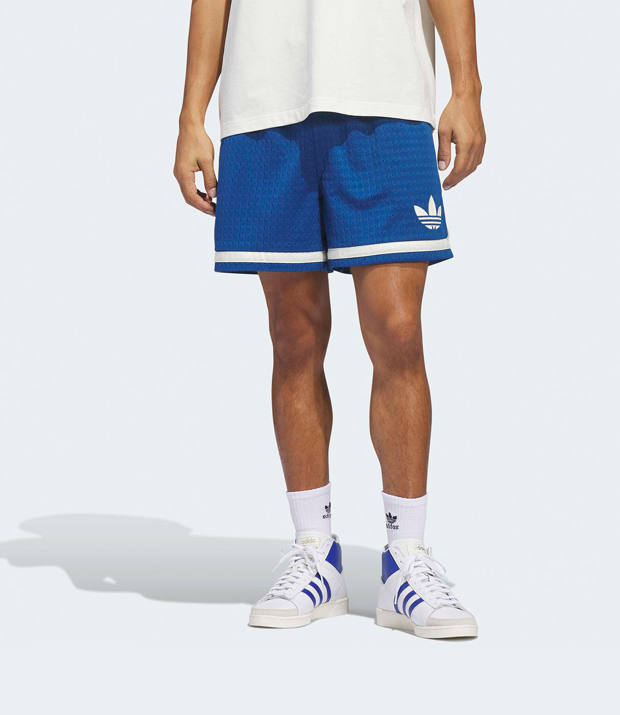 גבר לובש מכנסי ספורט קצרים בצבע כחול עם פס לבן, גרביים ונעלי סניקרס לבנות כחול