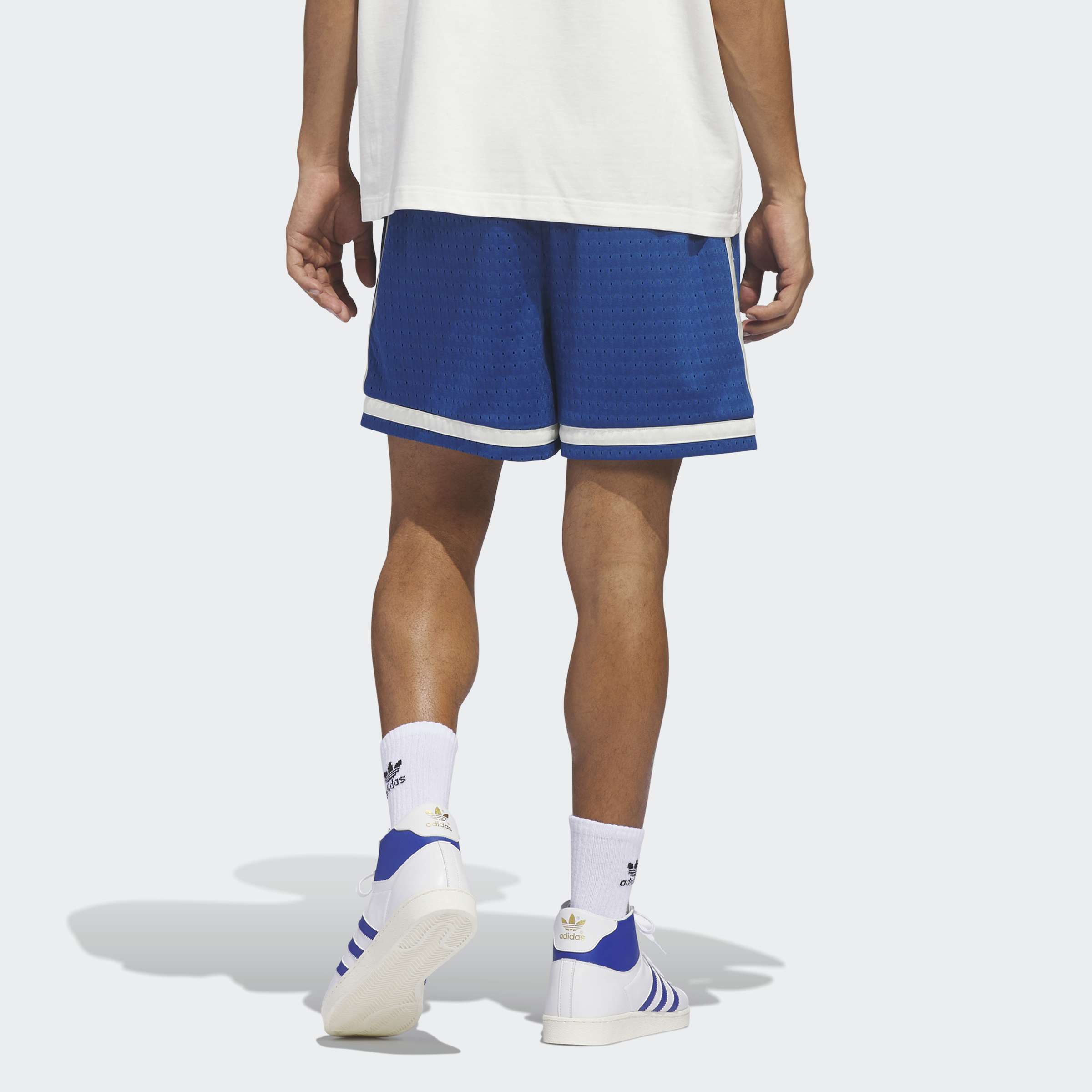 גבר לובש מכנסיים קצרים כחולים ובגדי ספורט, מבט מאחור, רקע בהיר