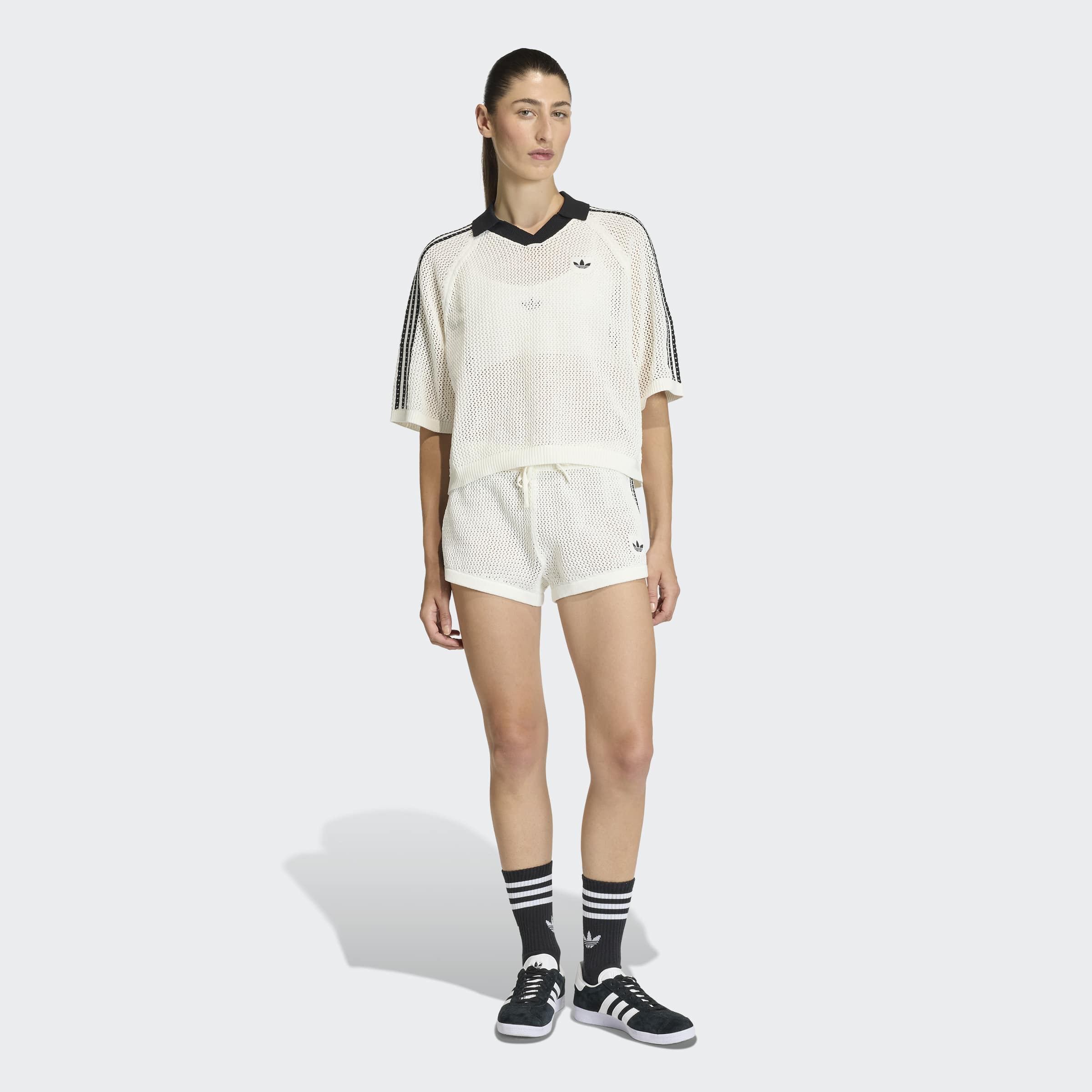 אישה לובשת סט ספורט רשת לבן, חולצה קצרה ומכנסיים קצרים, נעלי סניקרס גרביים שחורות