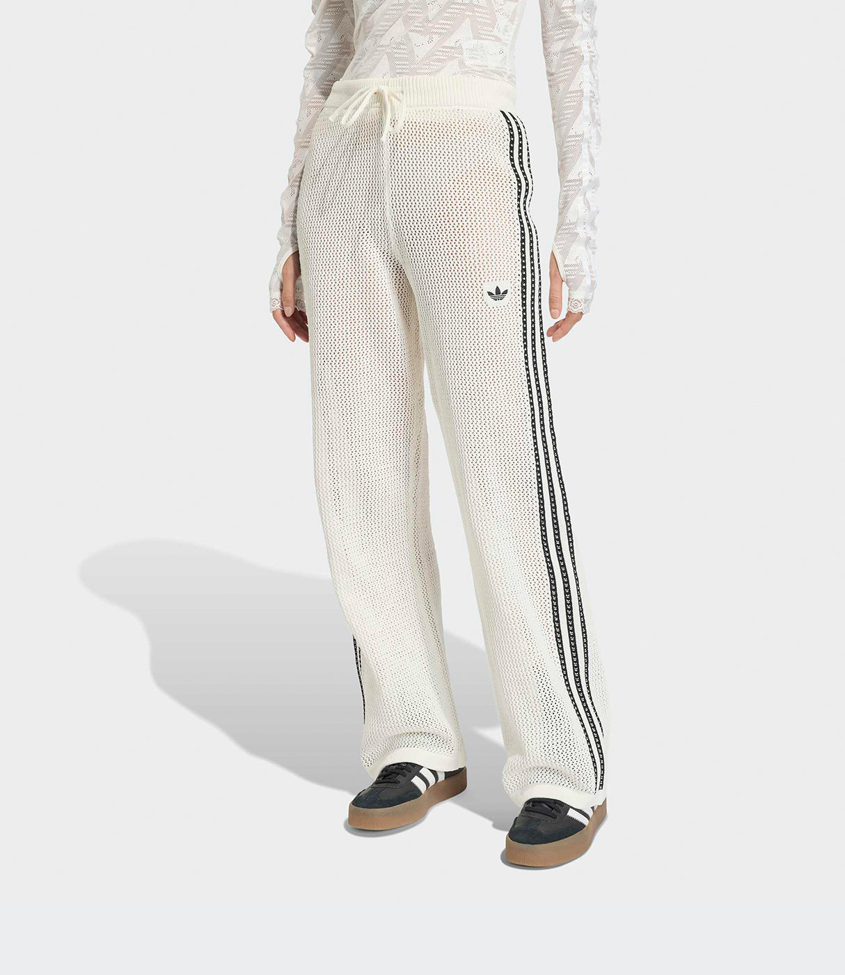 מכנסי נשים מחוררים בגוון שמנת עם פסים שחורים וסמל דגם אדידס, על דוגמנית עומדת