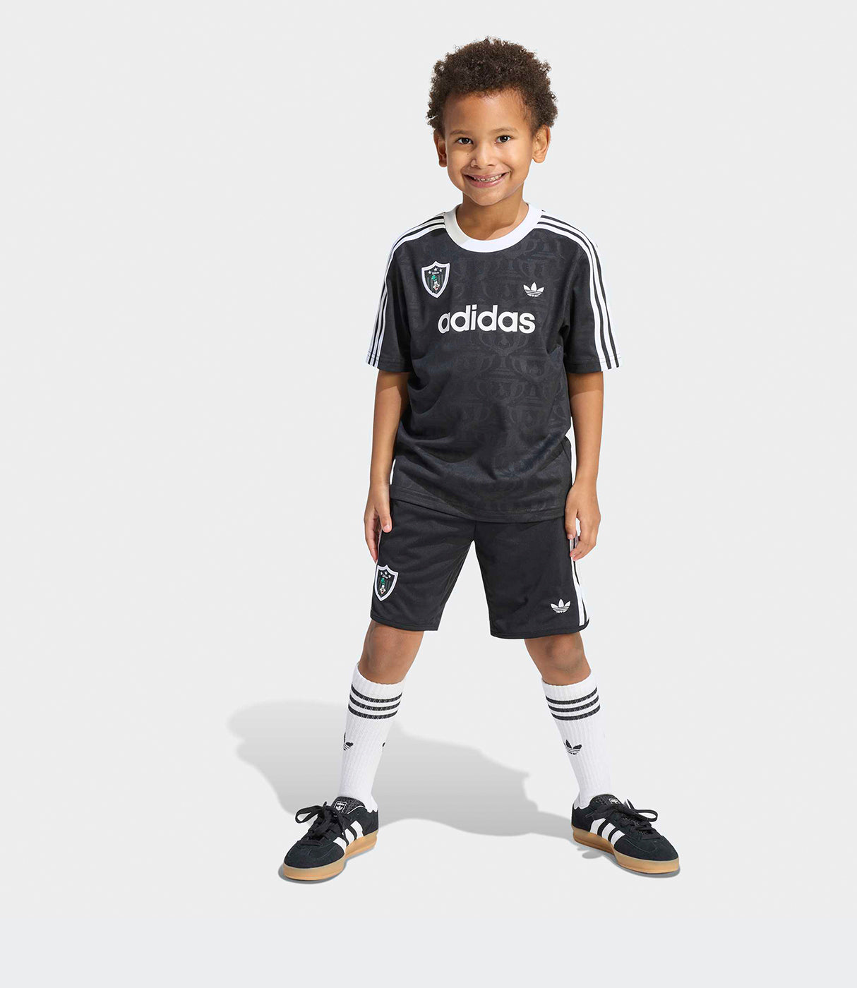 ילד לובש סט בגדי ספורט שחור של אדידס עם גרביים ונעליים תואמות על רקע לבן
