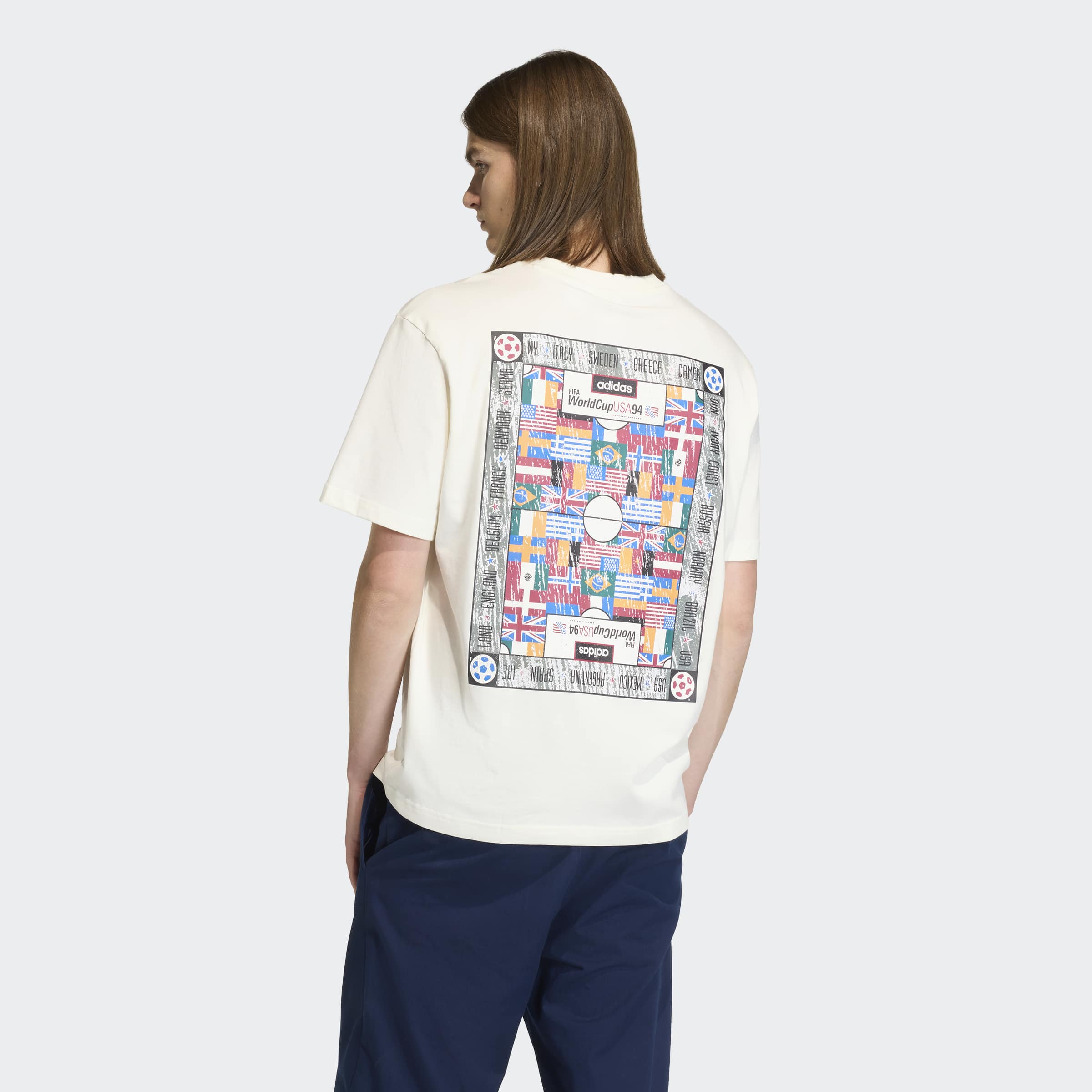 אדם לובש חולצת טי לבנה עם הדפס צבעוני של דגלים בגב, מכנסיים כחולים