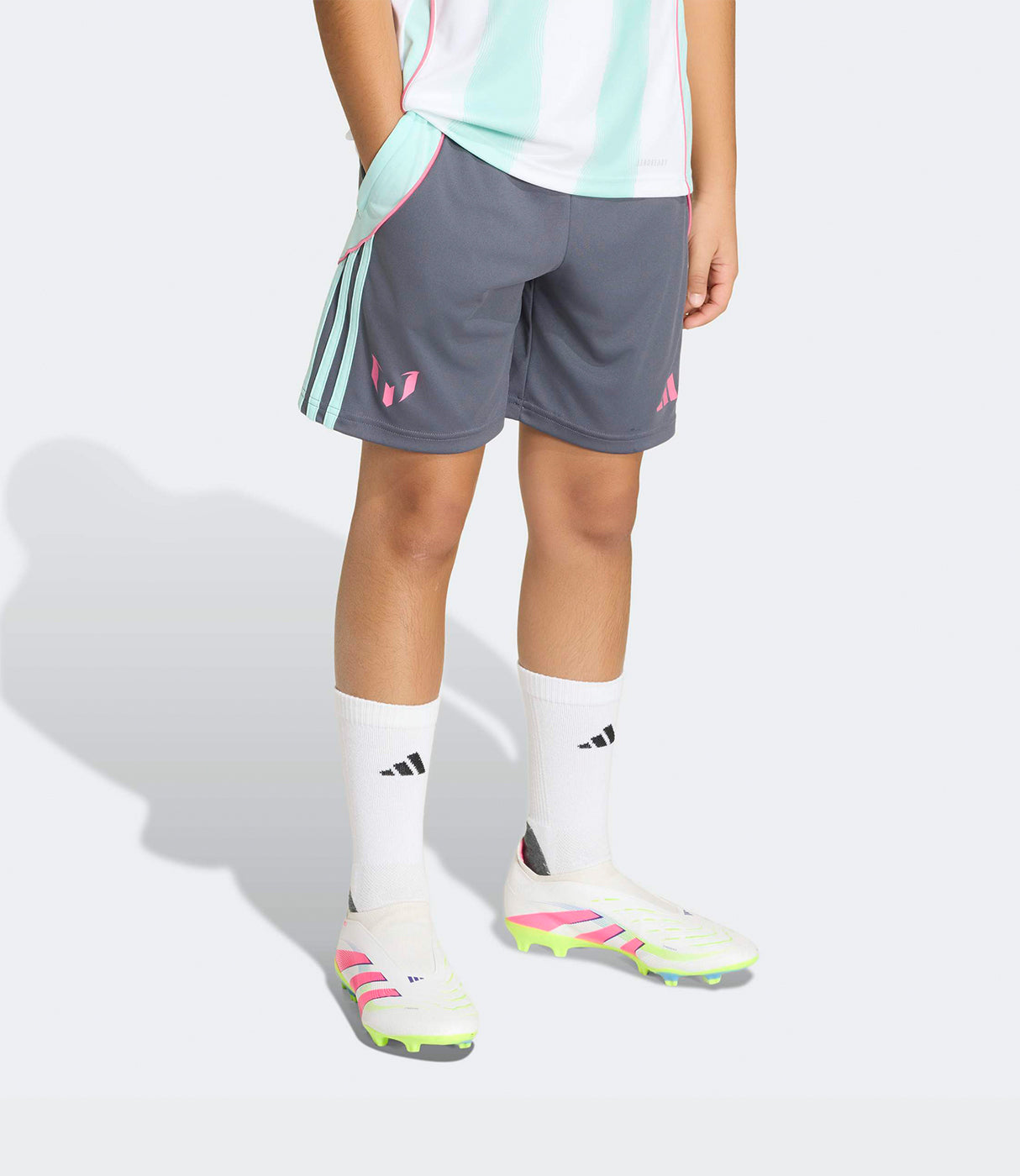 מכנסי ספורט קצרים לילדים בצבע אפור עם פסי טורקיז וסמל ורוד, לובשים עם גרביים ונעלי כדורגל