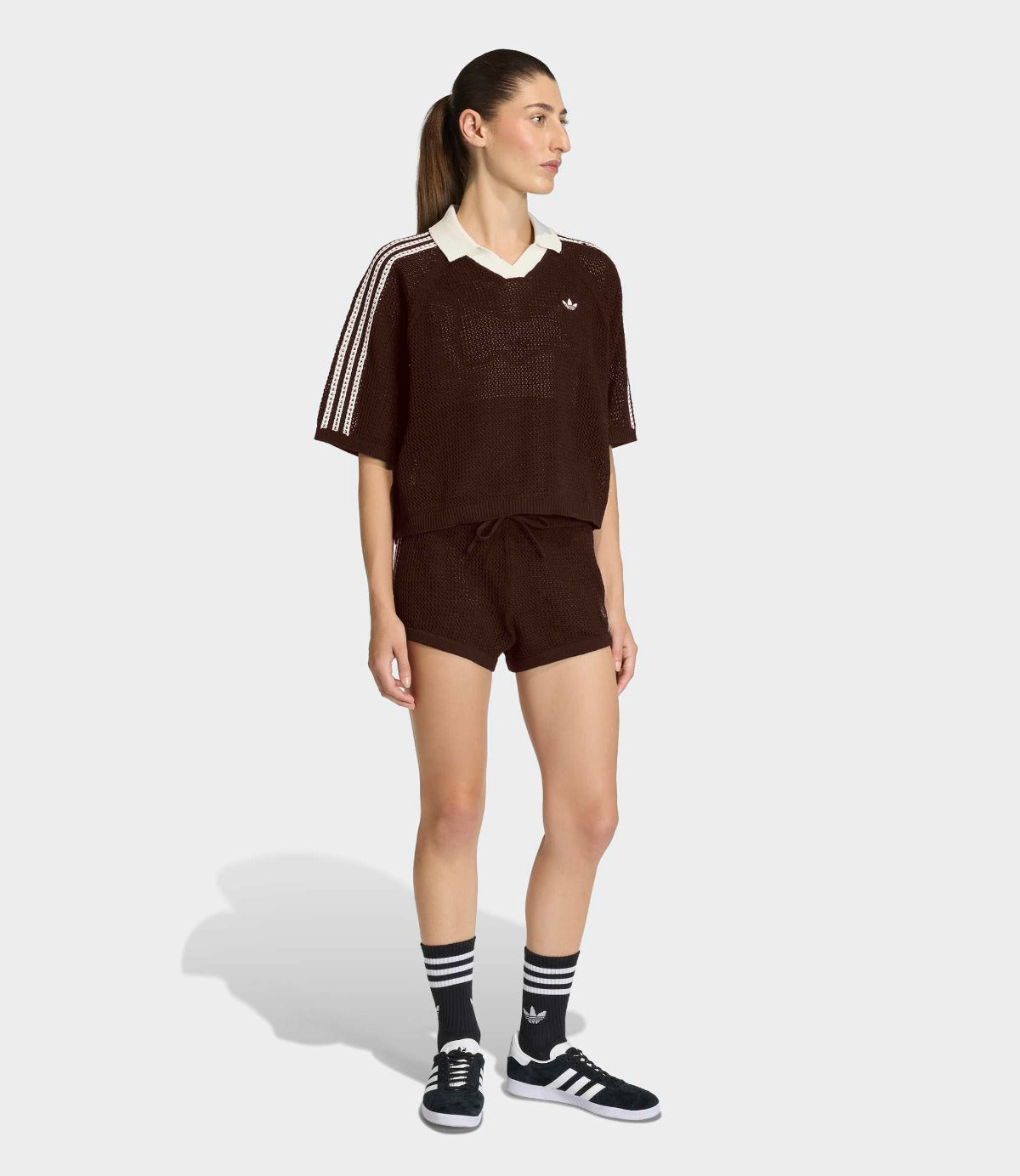 אישה לובשת סט ספורטיבי קצר בצבע כהה עם פסים לבנים בעיצוב מודרני, גרביים ונעלי סניקרס