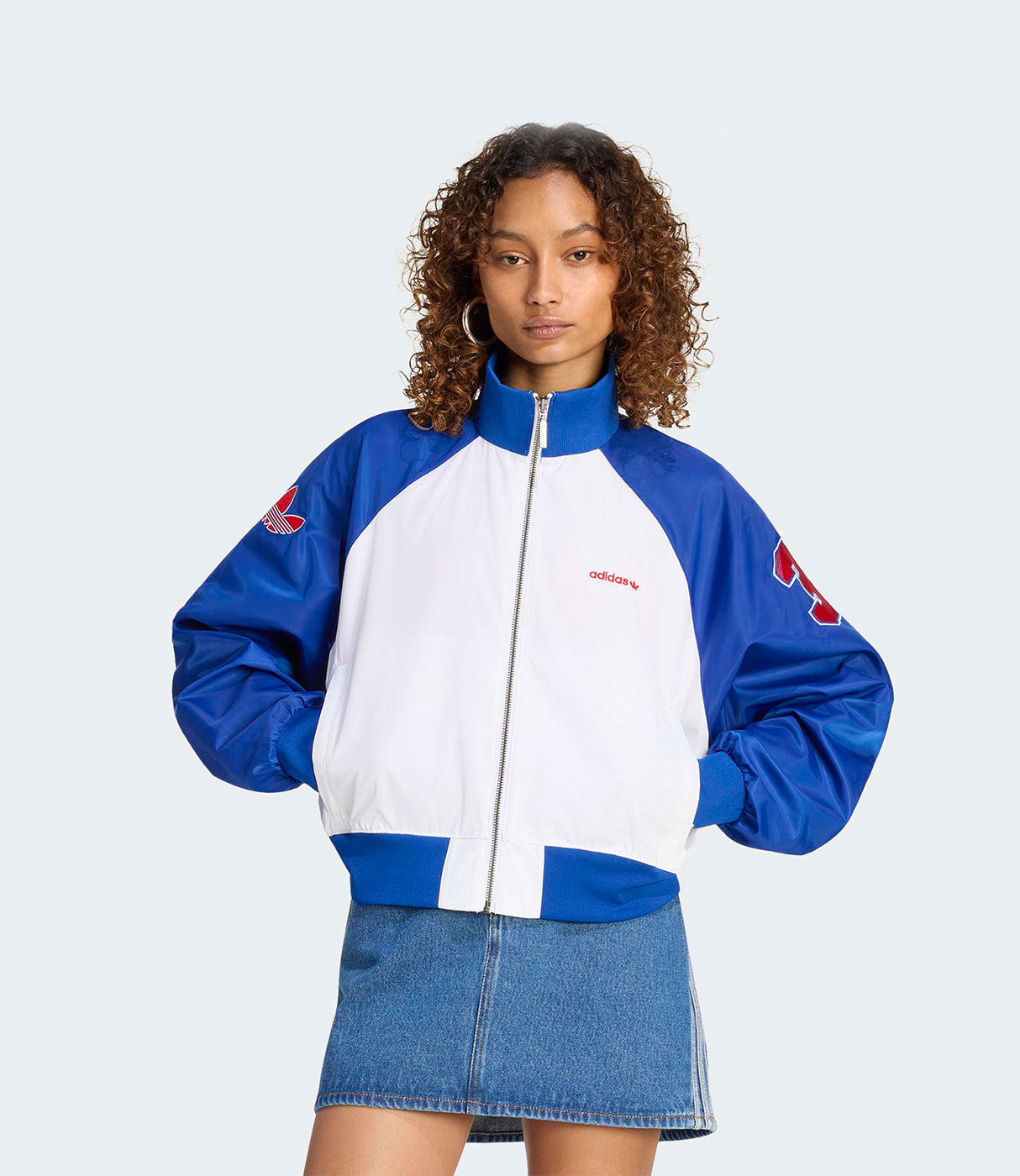אישה לובשת ג'קט ספורטיבי כחול לבן עם רוכסן וחצאית ג'ינס, רקע לבן