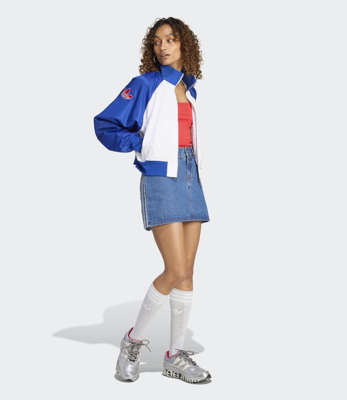 אישה עם ג'קט כחול-לבן, חצאית ג'ינס ונעלי ספורט בצבע אפור, לוק אופנתי יום יומי