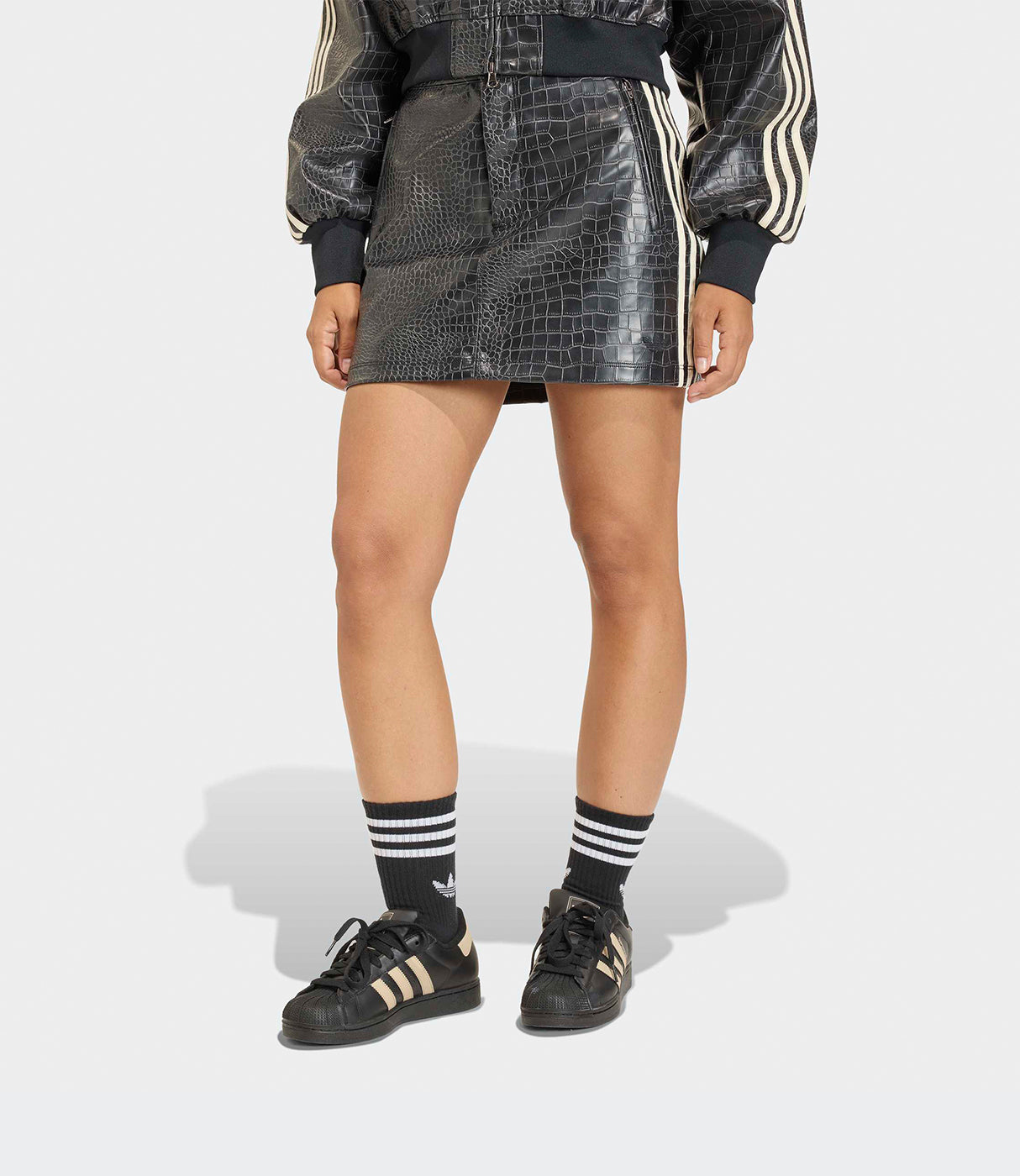 חצאית קצרה עם דוגמת עור תנין וספורט בלייזר, גרביים ונעלי ספורט שחורות, רקע אפור