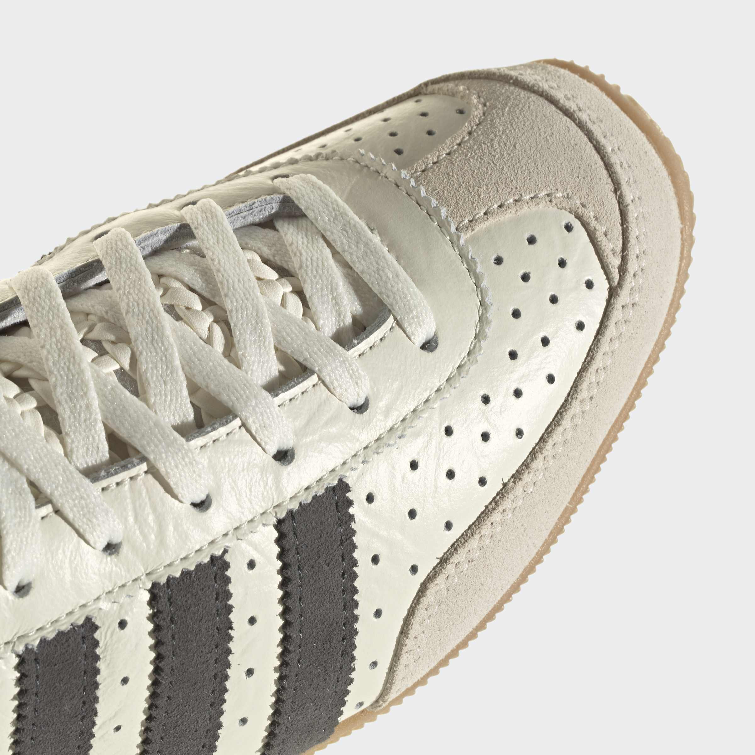 תקריב נעל ספורט אפורה עם פסים כהים, חירור ועיטורי זמש על החלק העליון