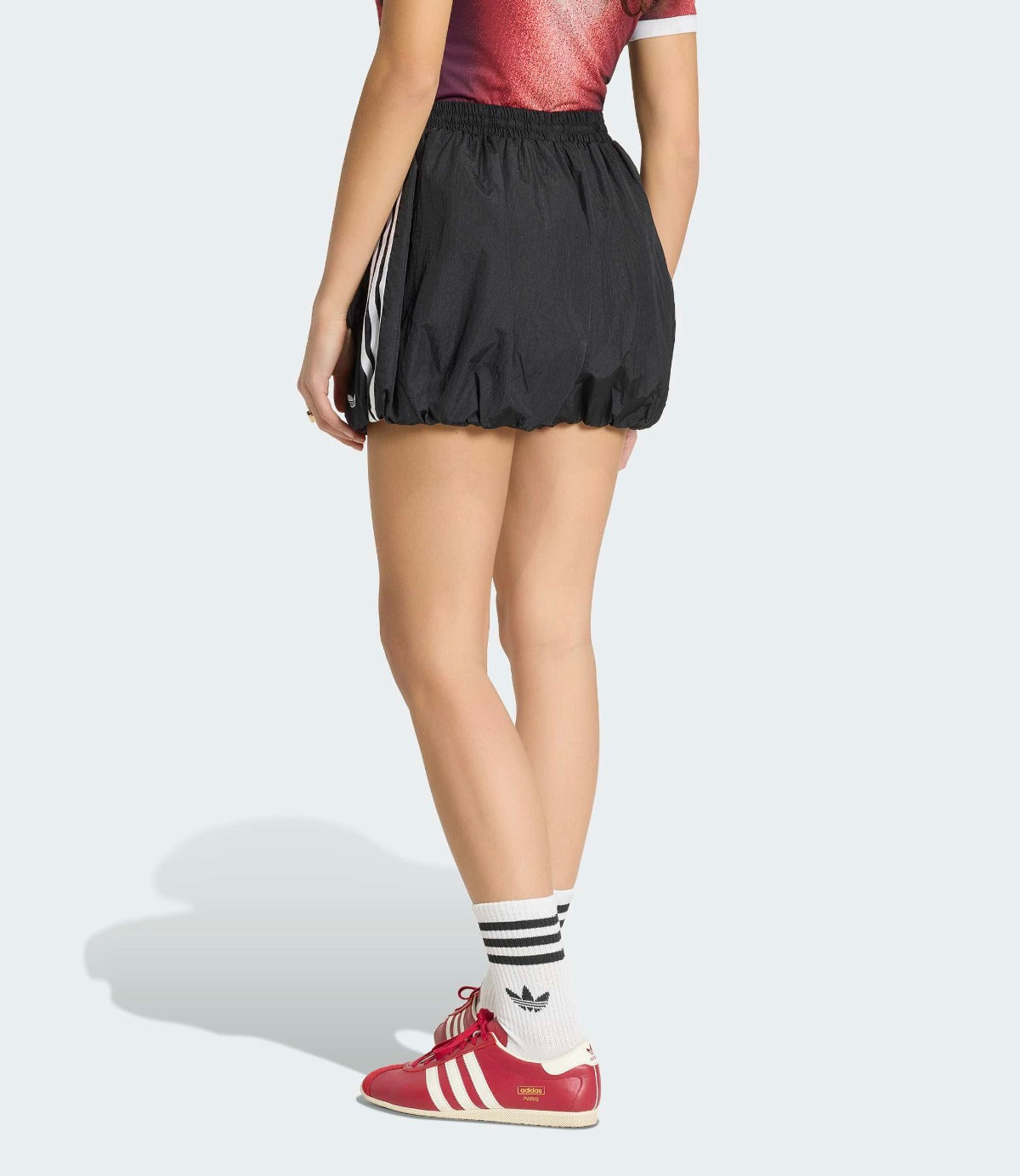 דגם לובש מכנסי ספורט קצרים שחורים עם פסים לבנים ונעלי אדידס אדומות, מבט מאחור