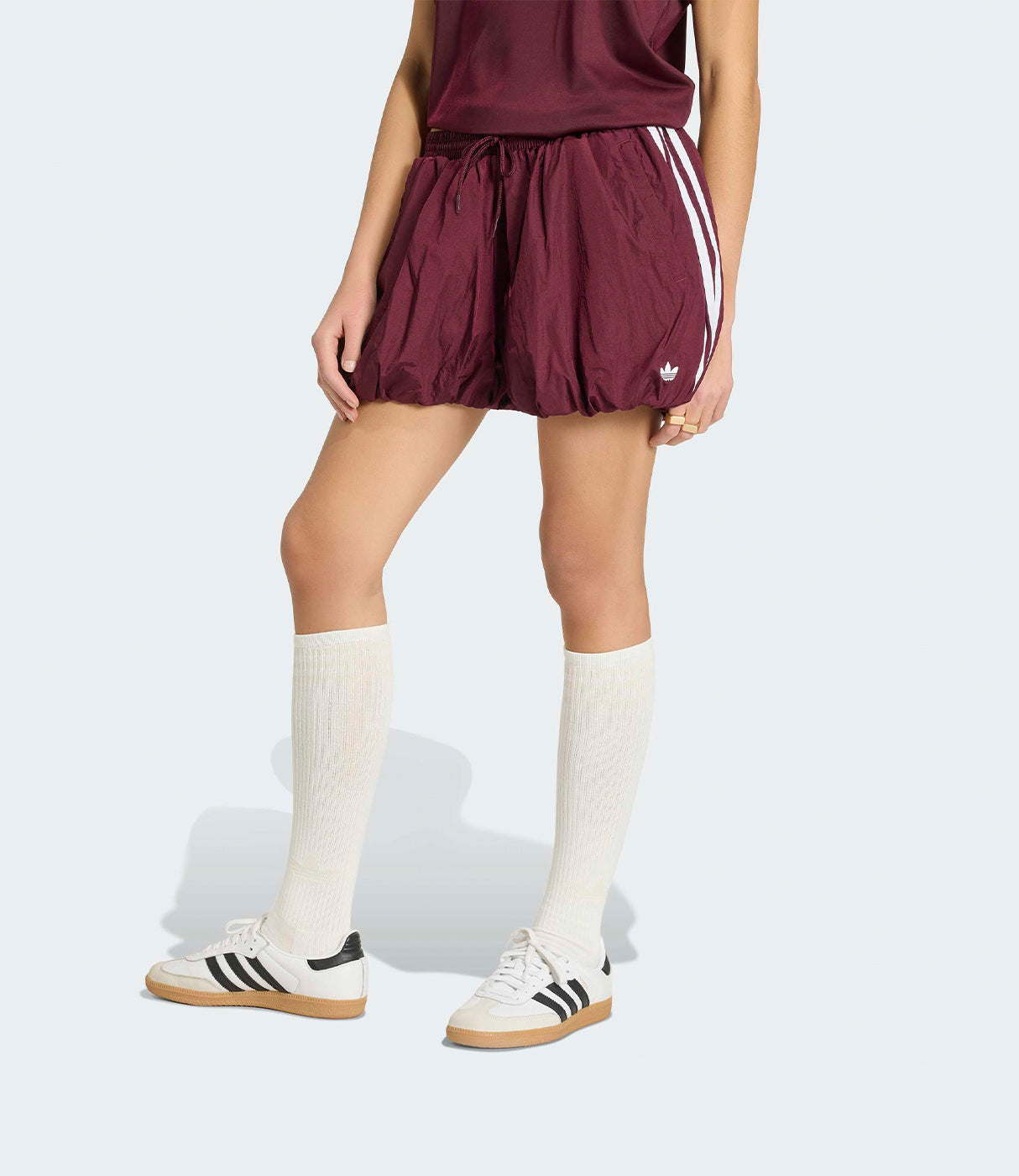 אישה לובשת מכנסי ספורט בורדו עם פסים לבנים, גרביים לבנות ונעלי ספורט אופנתיות