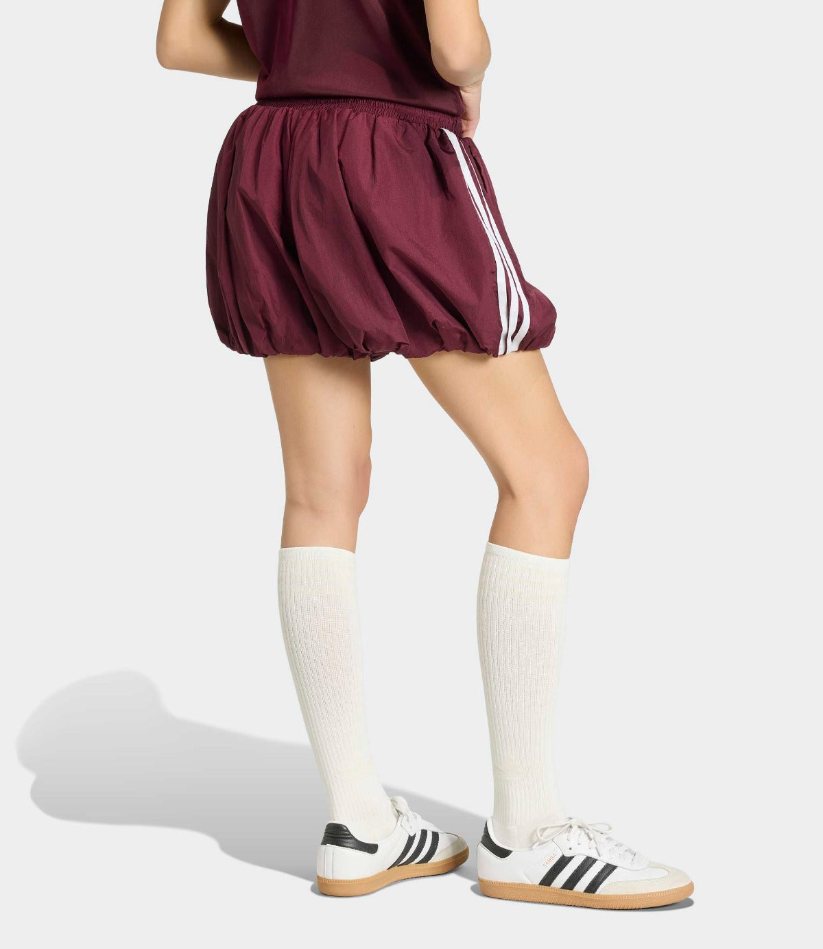 דוגמנית לובשת חצאית ספורט סגולה עם פסי צד לבנים, גרביים ארוכות ונעלי סניקרס לבנות