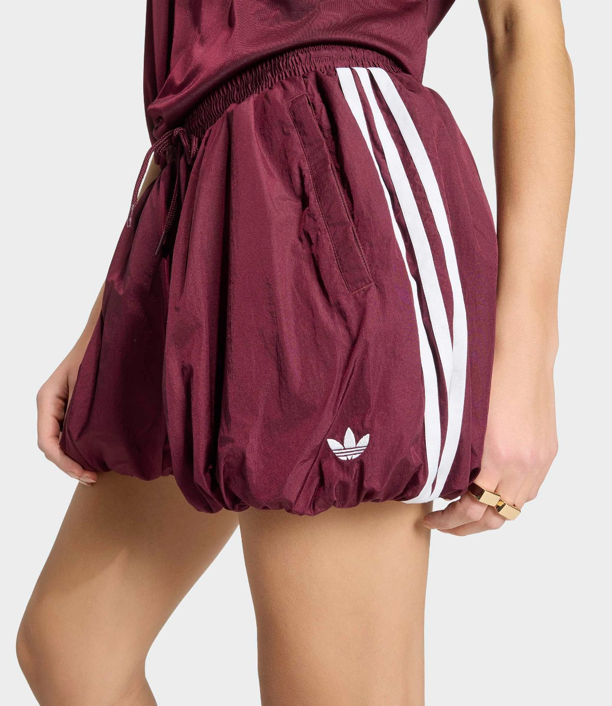 דוגמנית לובשת מכנסי ספורט בורדו עם שלושה פסים לבנים וסמל אדידס, מבד קליל