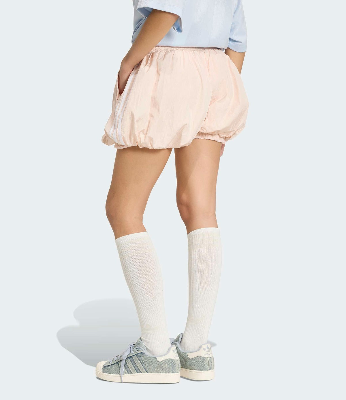 מבט אחורי על דוגמנית בלבוש קיץ: מכנסיים קצרים נפוחים בצבע בז', חולצה תכלת, גרביים לבנים ונעלי ספורט אפורות