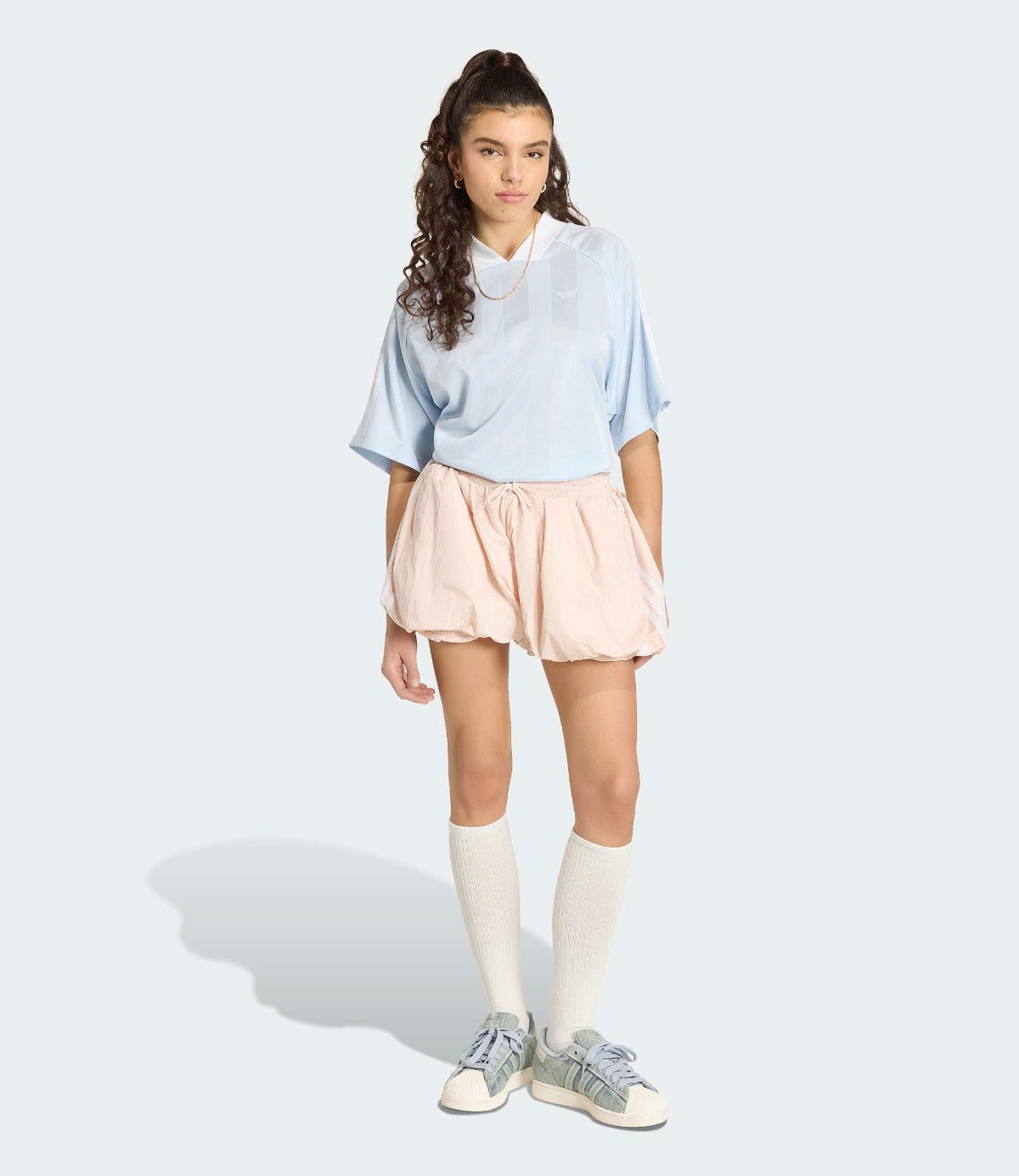 דוגמנית לובשת חולצה כחולה רחבה, חצאית קצרה בצבע בז' וגרביים גבוהות עם סניקרס אפורות