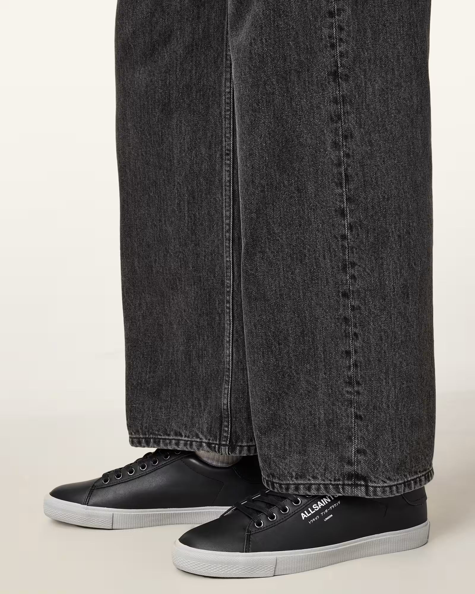 ג'ינס שחור רחב ונעלי סניקרס שחורות עם שרוכים וסוליה לבנה, כתובת ALLSAINTS על הנעל