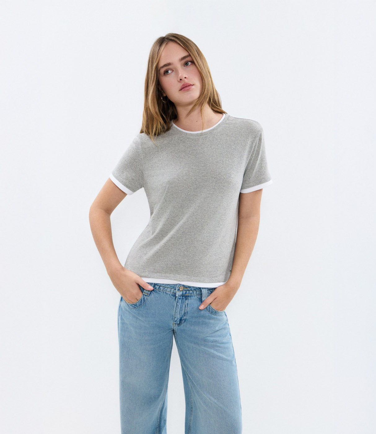 אישה לובשת טי שירט אפורה עם שרוולים קצרים ומכנסי ג'ינס בהירים, רקע לבן