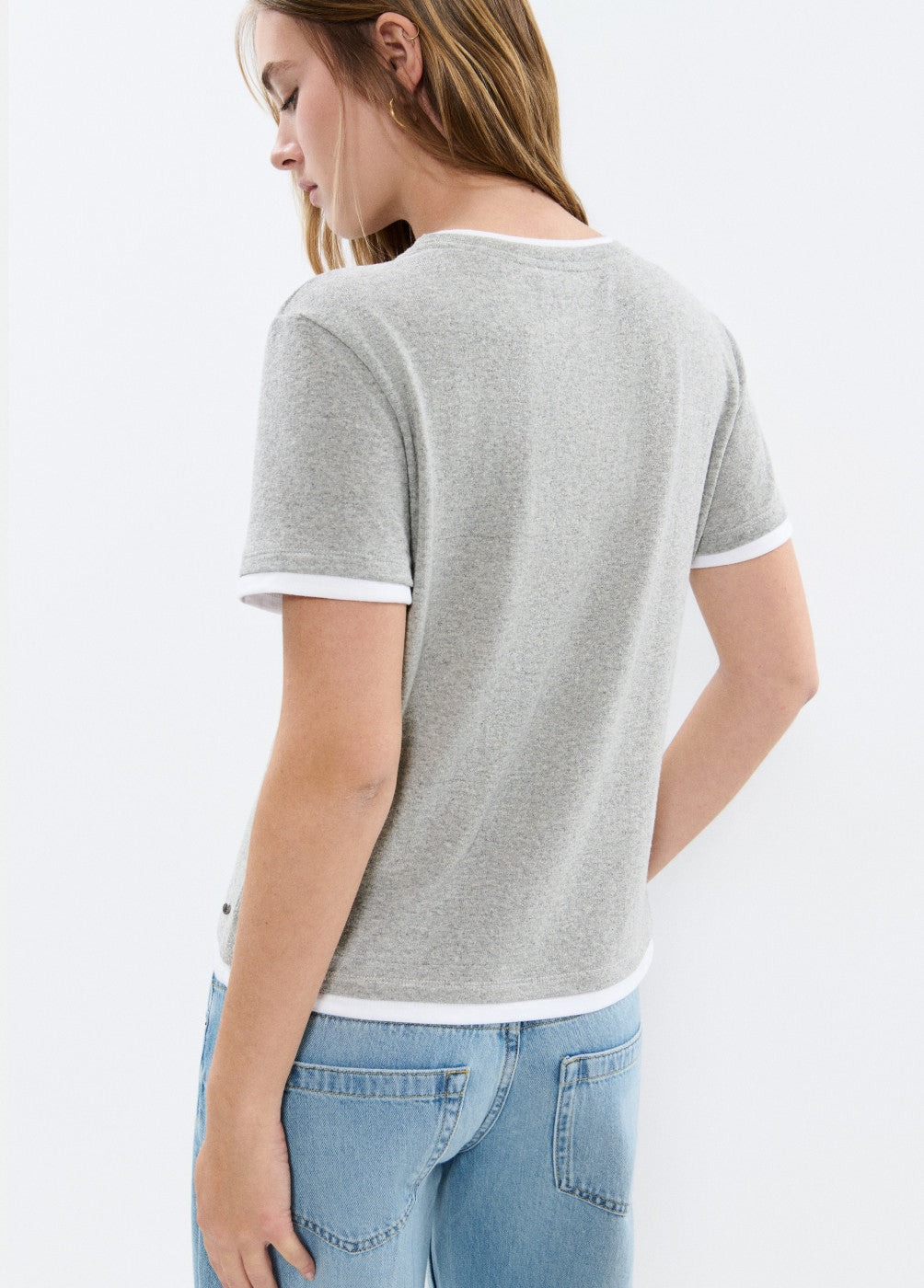 אישה לובשת חולצת טי קצרה אפורה עם תפרים לבנים ומכנסי ג'ינס בהירים, בצילום מהגב