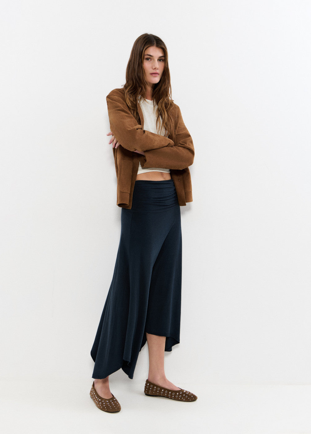 אישה לובשת חצאית שחורה מתנפנפת, חולצה קצרה, ז'קט חום ונעליים שטוחות חומות