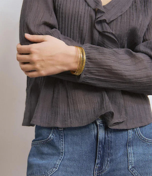 אישה עם צמידי זהב אופנתיים של CHOZEN, חולצה אפורה ומכנסי ג'ינס