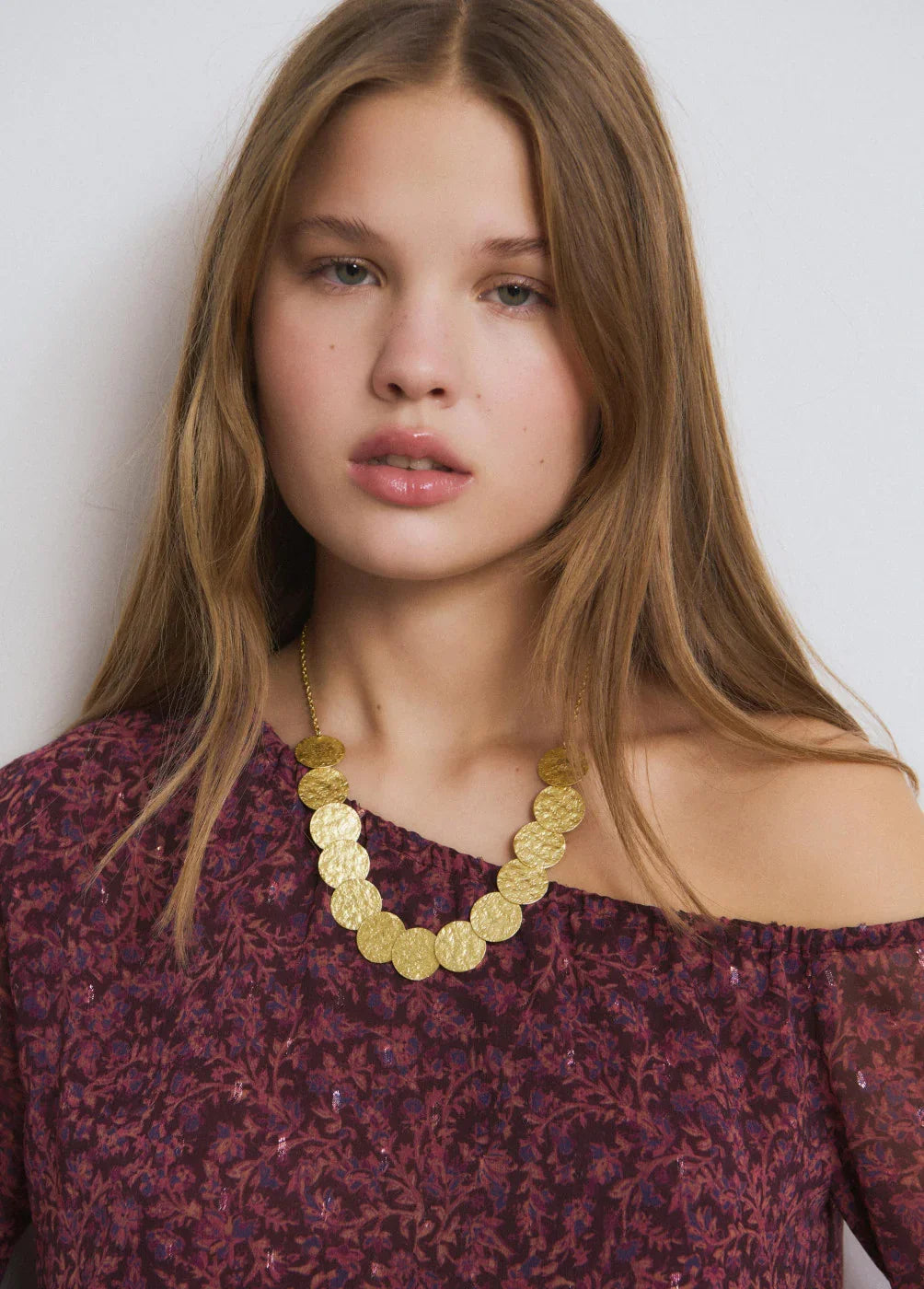 דוגמנית עם שיער בלונדיני עונד שרשרת זהב עגולה, לובשת חולצה סגולה עם הדפס, צילום לאתר CHOZEN