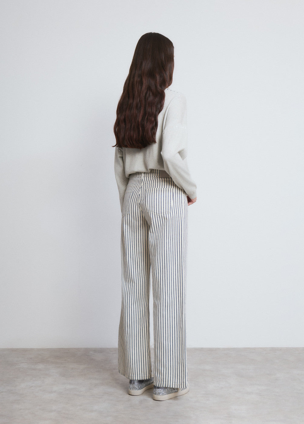 דוגמנית עם מכנסיים מחויטים פסים רחבים וסוודר בהיר, צילום אופנה באולפן