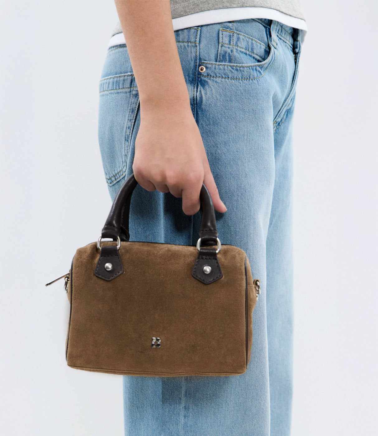 תיק יד חום קטן עם ידיות שחורות, מוחזק ביד, לצד ג'ינס כחול