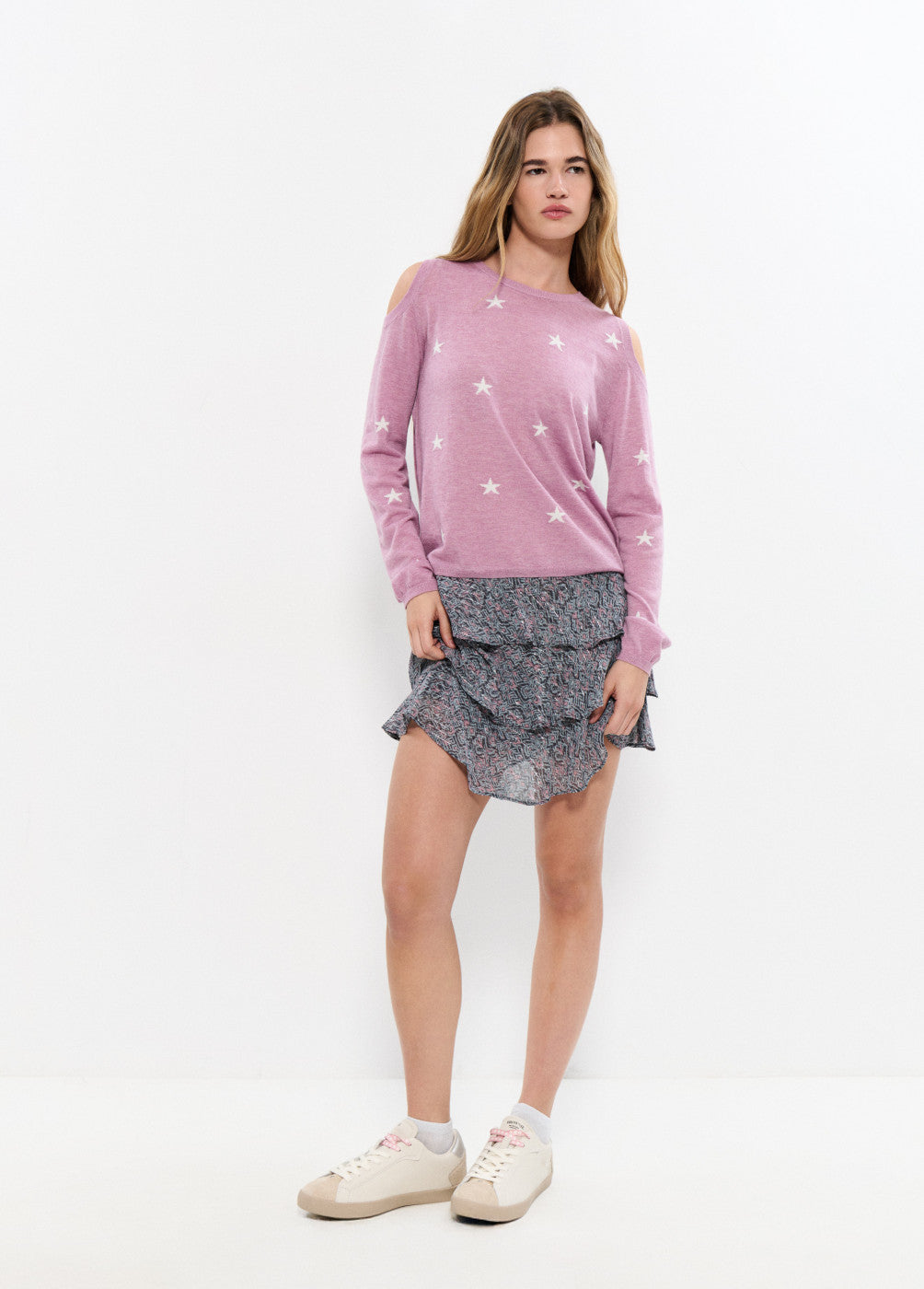 אישה לובשת סוודר ורוד עם כוכבים וחשיפת כתפיים וחצאית פרחונית קצרה