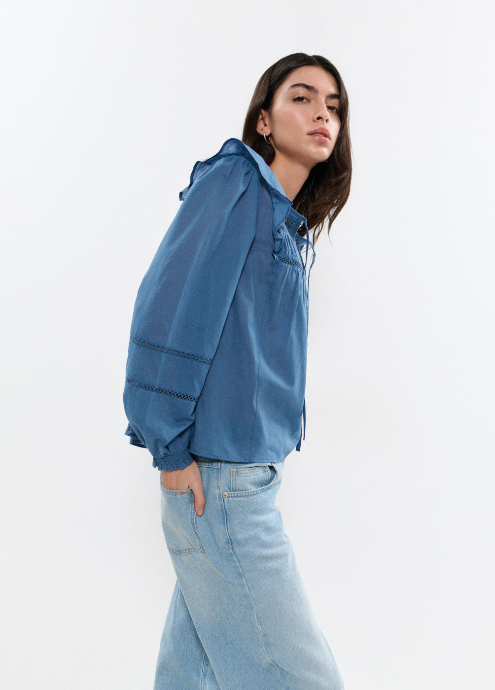 אישה עם חולצת ג'ינס כחולה שרוולים ארוכים ועיצוב קפלים, ג'ינס בהיר, רקע לבן