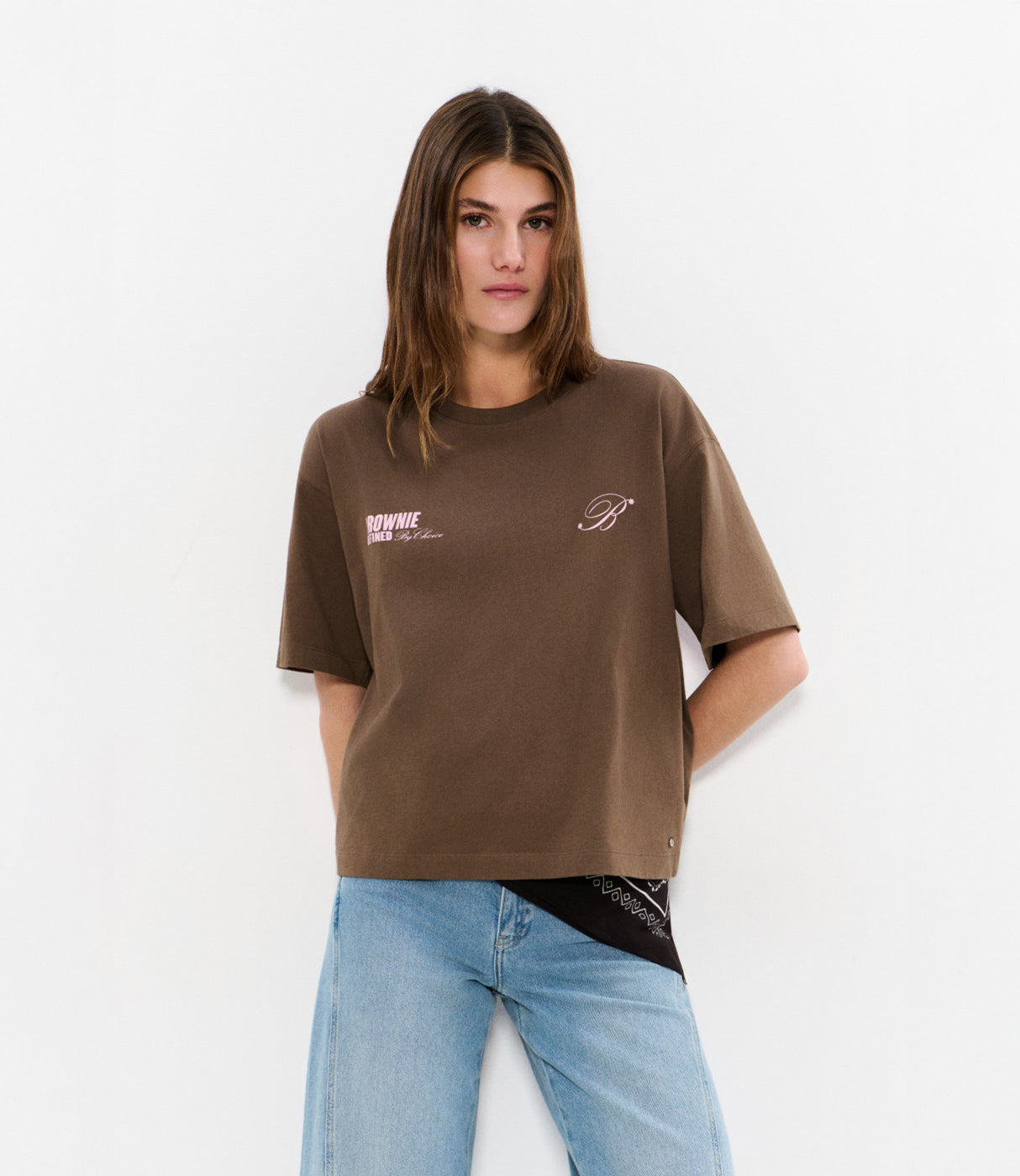 אישה לובשת חולצת טי חומה עם הדפס ורוד ומכנסי ג'ינס, צילום אופנה על רקע לבן