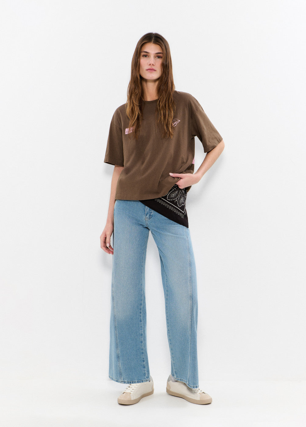 אישה לובשת חולצה חומה רחבה, ג'ינס רחב ונעלי סניקרס, סטייל אופנתי יומיומי