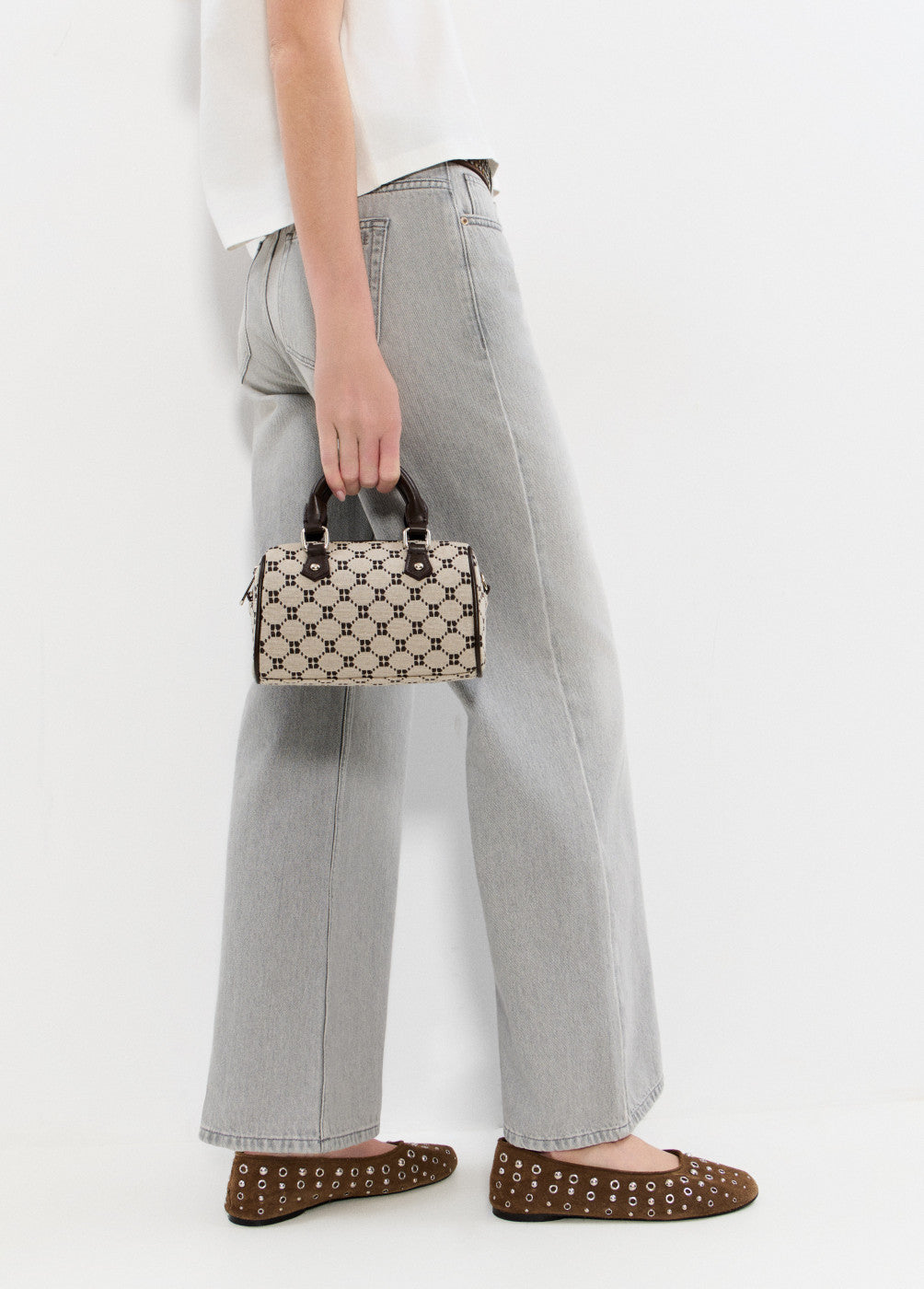 אישה עם ג׳ינס אפור, מחזיקה תיק יד קטן בדוגמת שחור-לבן, ונועלת נעליים שטוחות חומות עם ניטים