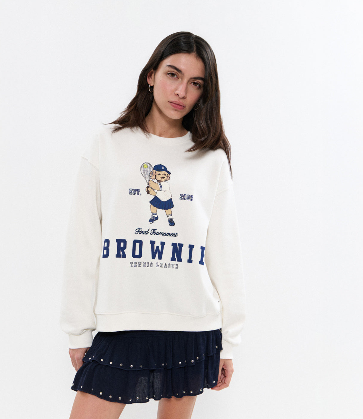 דוגמנית לובשת סווטשירט לבן עם הדפס דובי טניס ומכפלת חצאית כחולה
