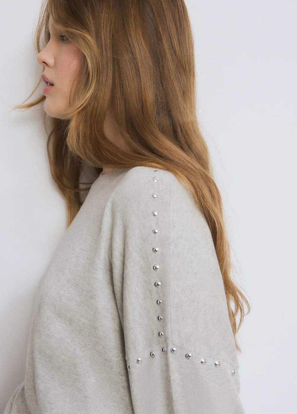 אישה עם סוודר אפור בעל ניטים כסופים, אופנה מבית CHOZEN, קבוצת אלפא