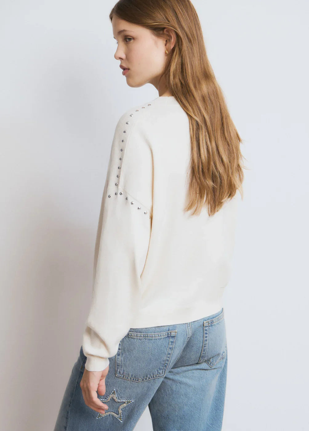 דוגמנית לובשת סוודר לבן עם ניטים בגב וג'ינס תכלת, אופנה טרנדית CHOZEN