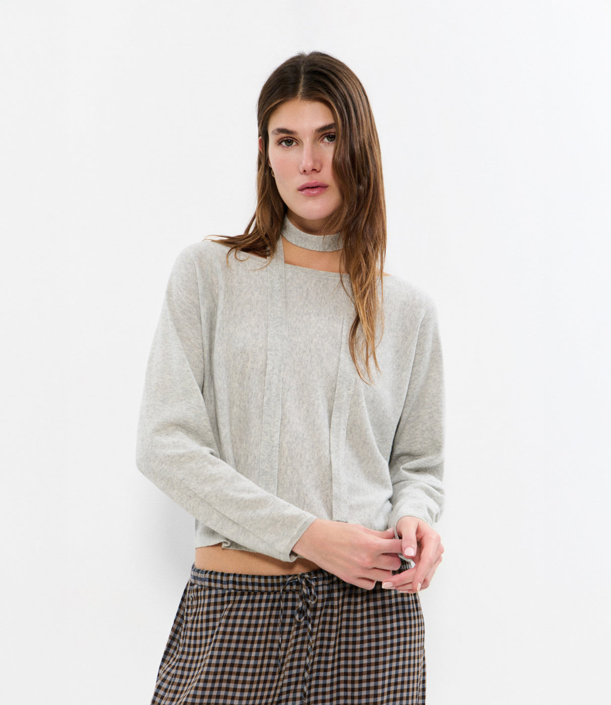 אישה לובשת חולצה אפורה עם שרוולים ארוכים ומכנסיים משובצים, רקע לבן