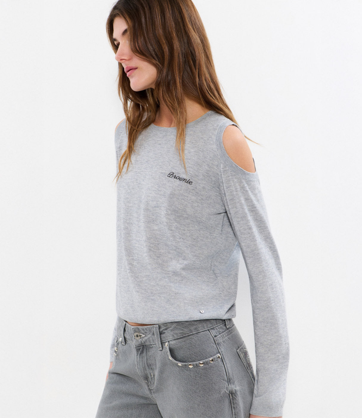 אישה לובשת חולצת כתפיים חשופות בצבע אפור בהיר ומכנסי ג'ינס אפורים אופנתיים