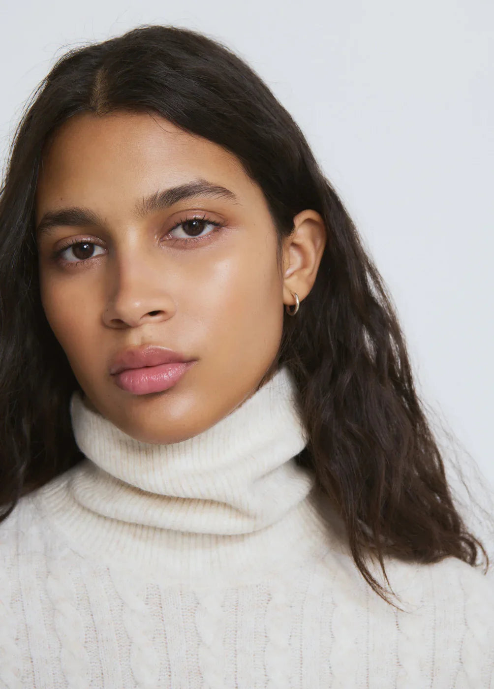 אישה צעירה עם שיער כהה לובשת סוודר לבן עם צווארון גולף, רקע בהיר, צילום אופנה CHOZEN