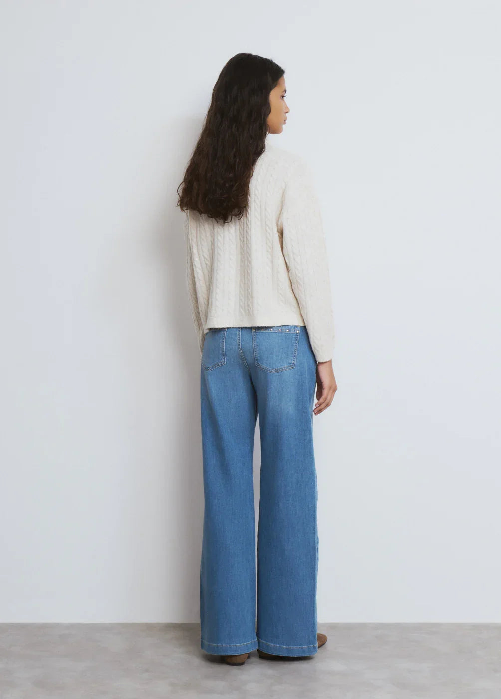 דוגמנית לובשת סוודר שמנת ומכנסי ג'ינס רחבים, בסטייל אופנתי של CHOZEN