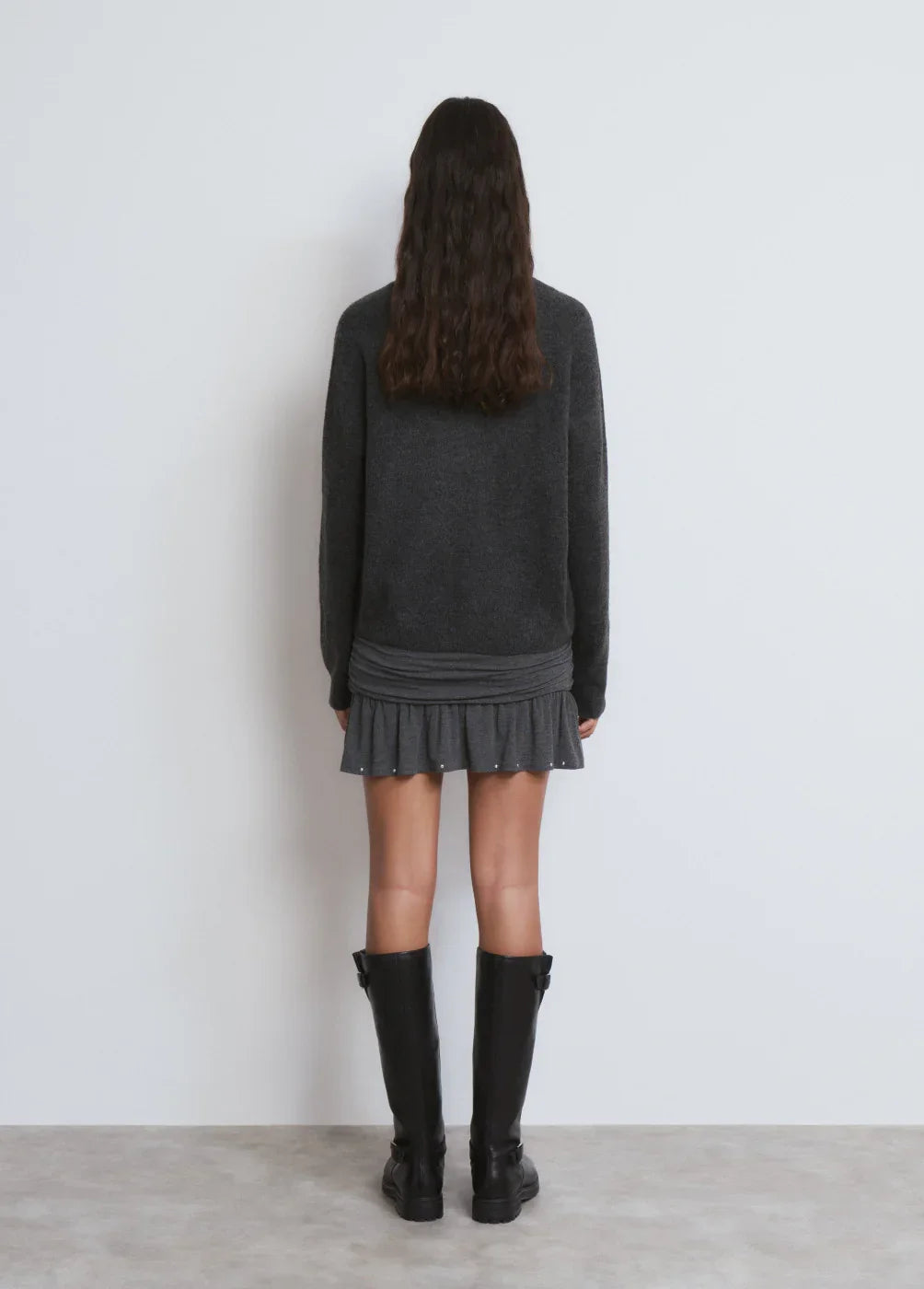 אישה עם סweater אפור, חצאית אפורה קצרה ומגפיים שחורים, עומדת עם הגב, CHOZEN אופנה