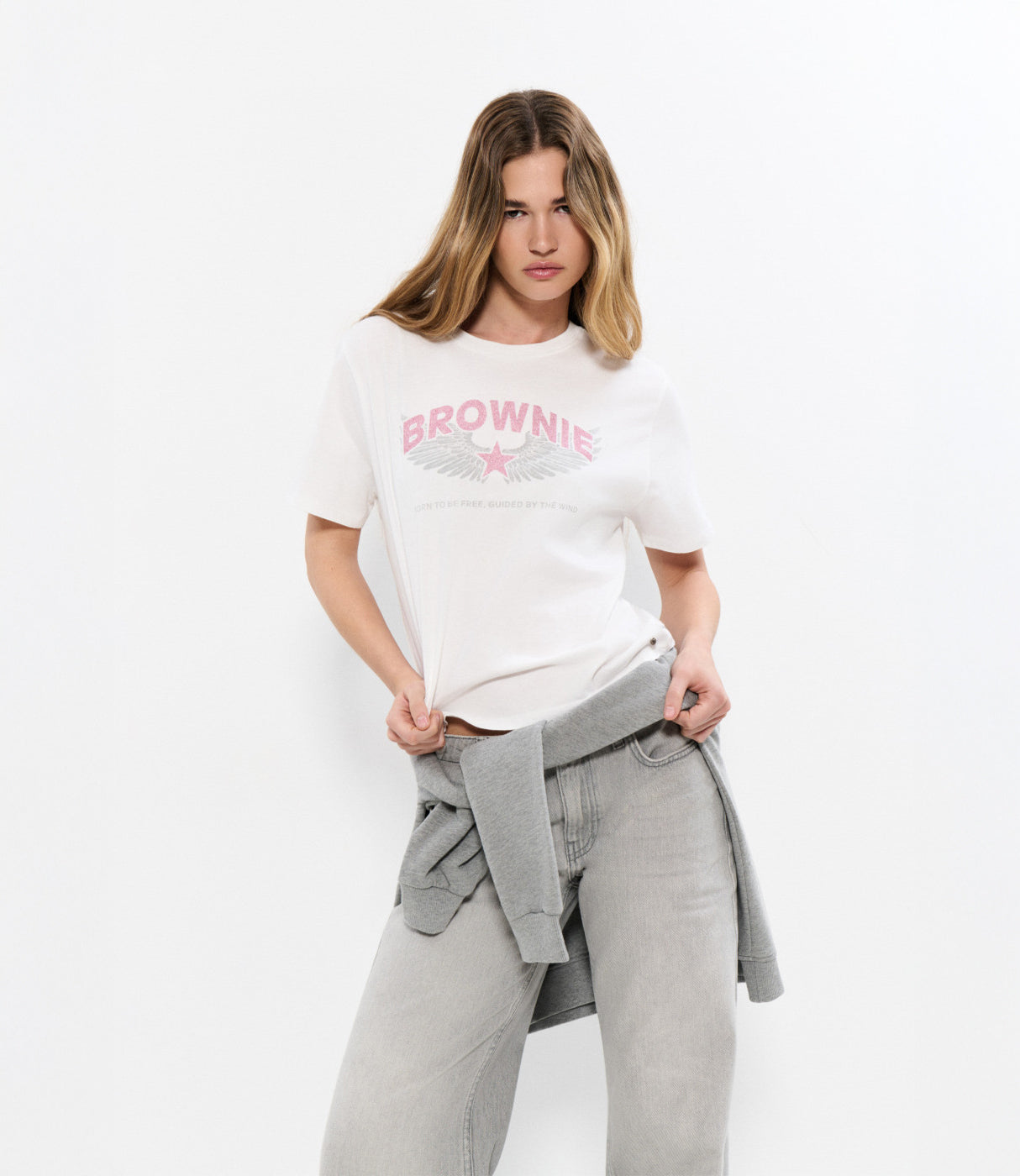 דוגמנית לובשת חולצה לבנה עם כיתוב BROWNIE ומכנסי ג'ינס אפורים, סטייל קז'ואל