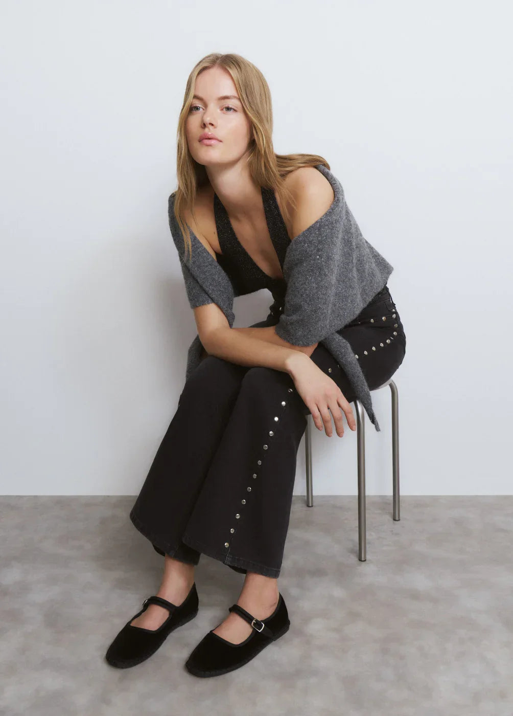 אישה בלבוש אופנתי יושבת על כיסא, בגדים כהים עם ניטים, צילום ל-CHOZEN מותגים מובילים